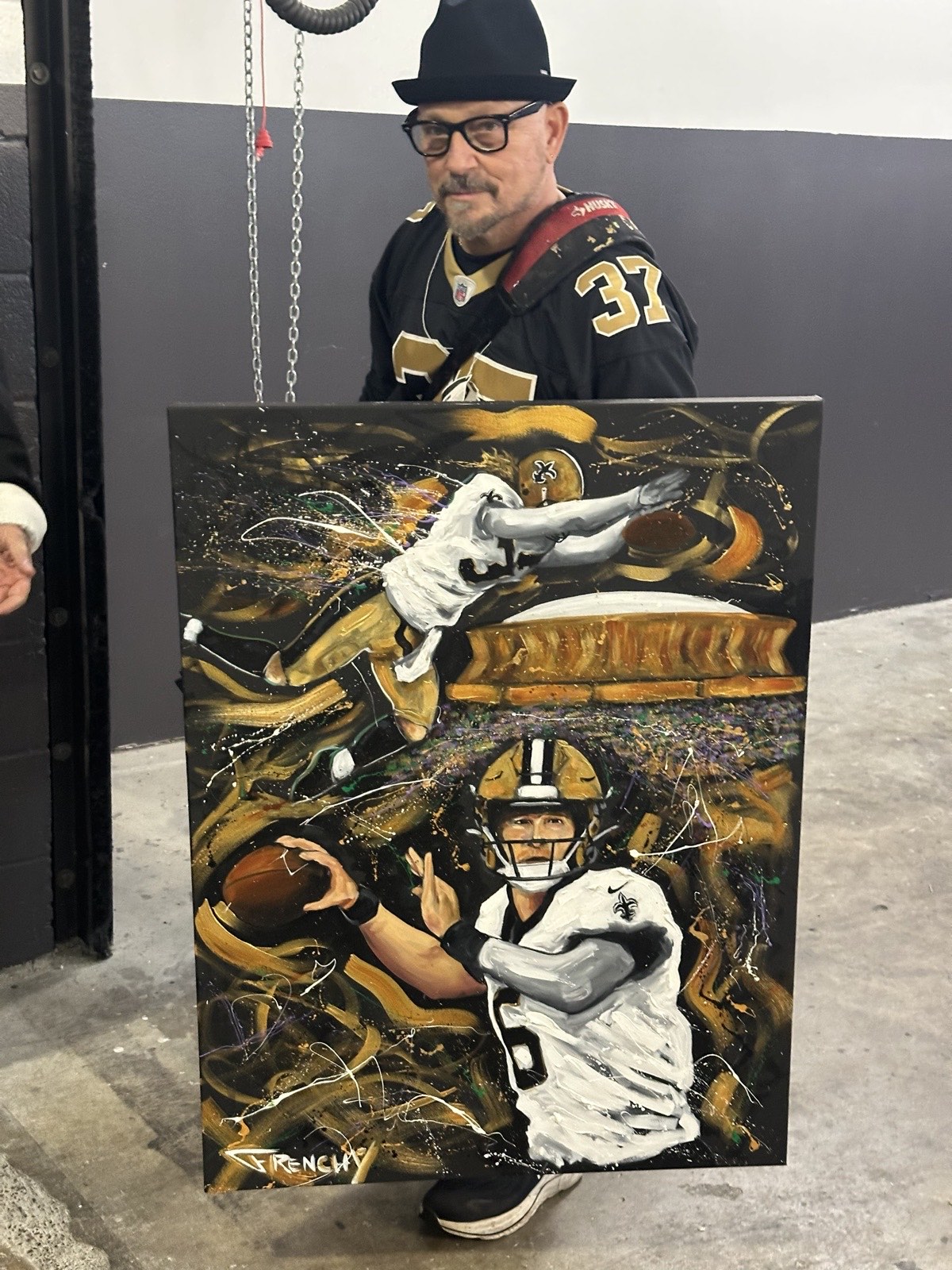 Frenchy on the Saints sideline with the finished painting, wearing a #37 jersey