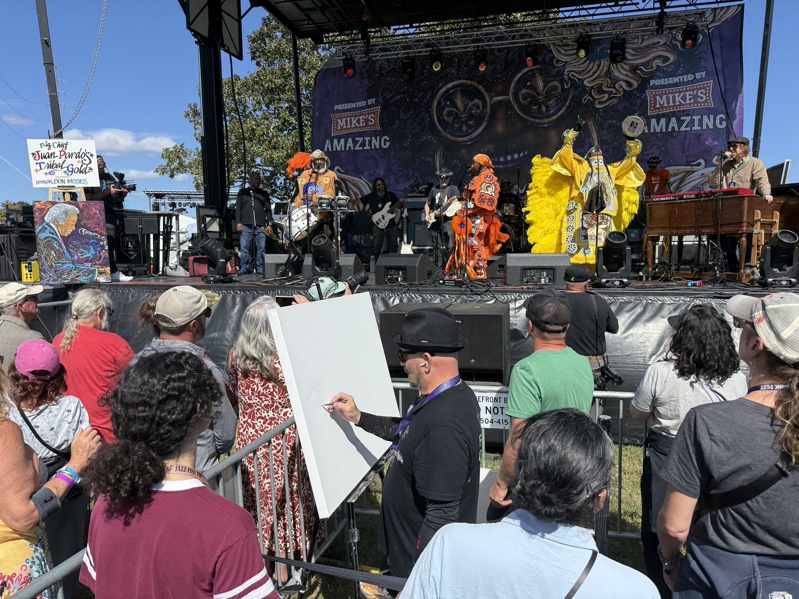 Frenchy painting in front of the stage during Big Chief Juan Pardo's Tribal Gold, with Mardi Gras Indian suits in yellow and orange on stage